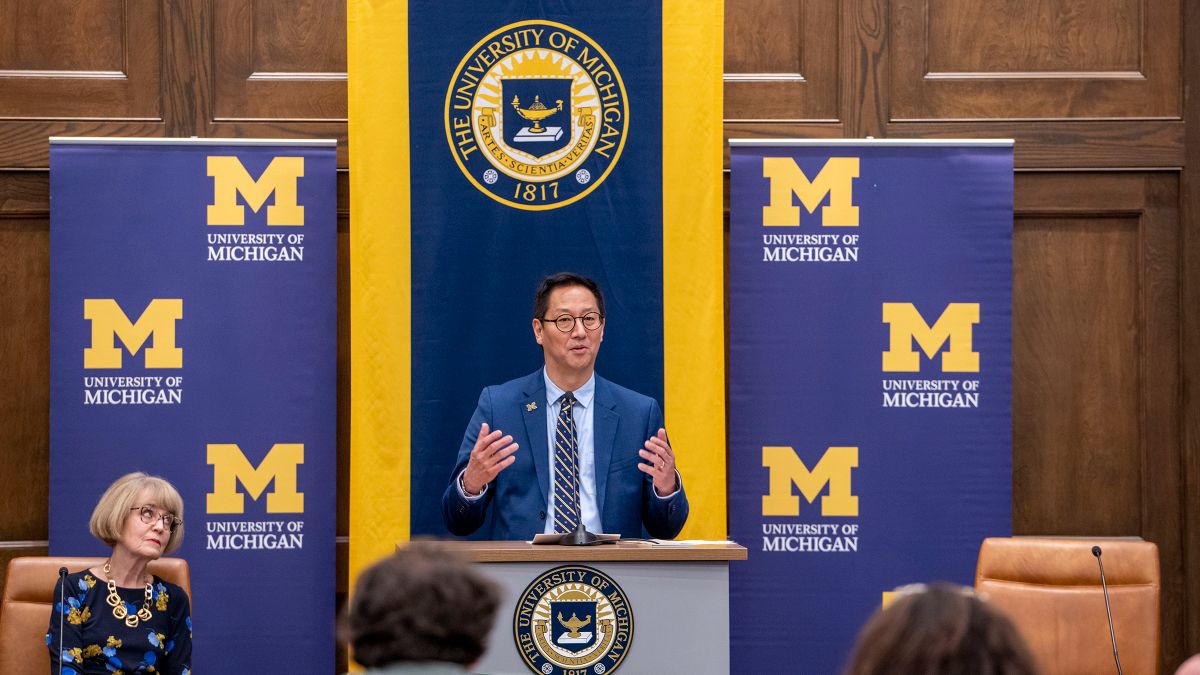 New University of Michigan President Santa Ono stands behind a podium and in front of a background bearing university logos.